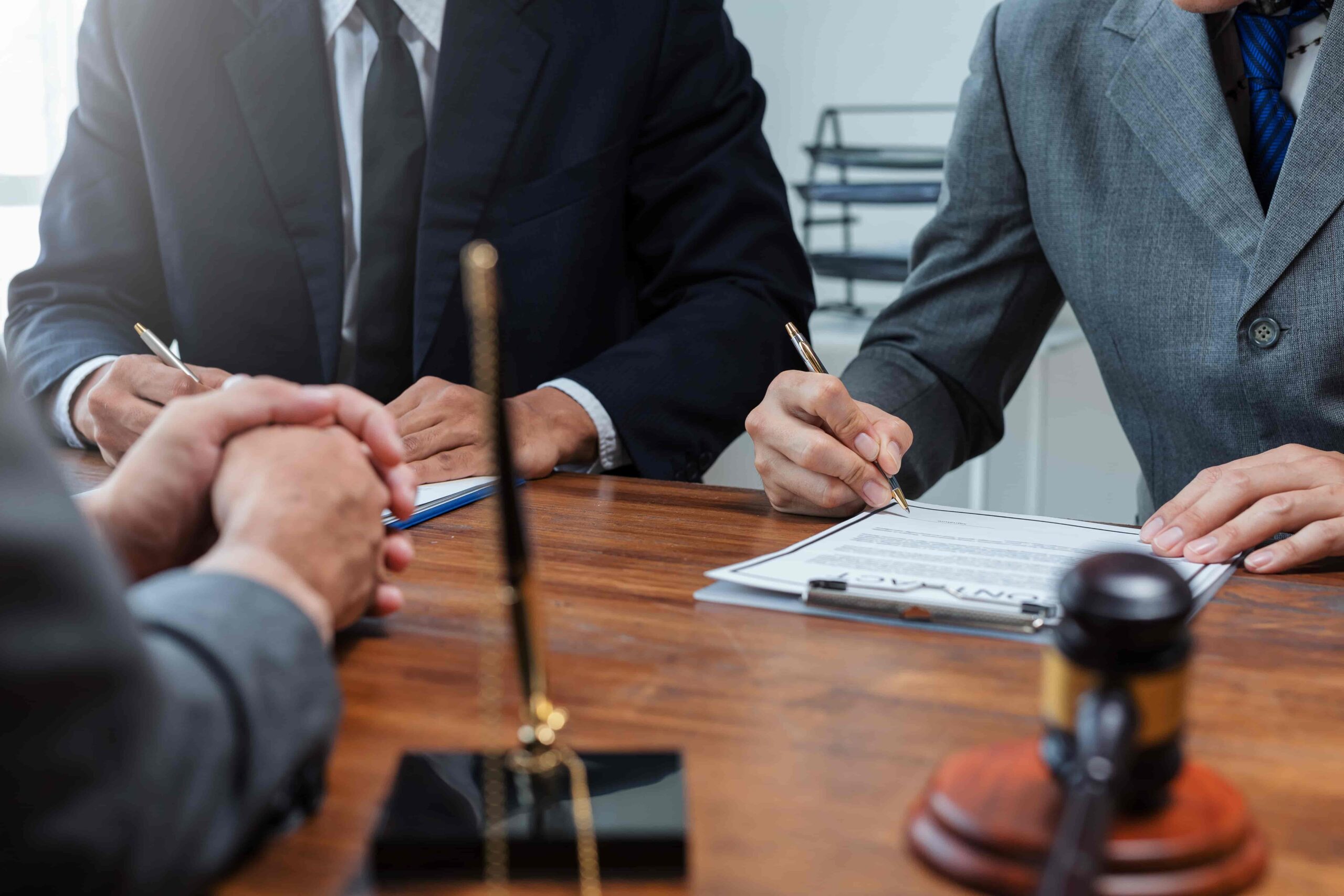 Lawyers reviewing and signing a legal contract during a client meeting at a desk with gavel and legal documents, representing legal consultation and agreement